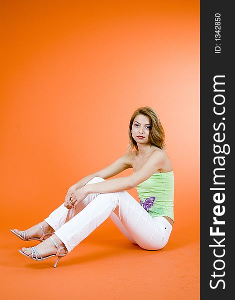 Blond girl relaxing on the floor; wearing casual clothes; orange background. Blond girl relaxing on the floor; wearing casual clothes; orange background