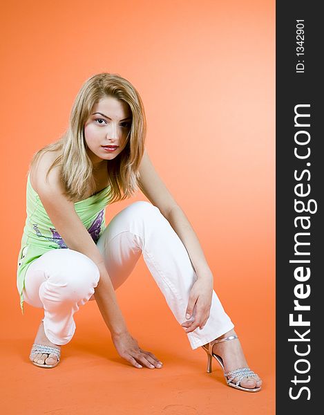 Blond girl relaxing on the floor; wearing casual clothes; orange background. Blond girl relaxing on the floor; wearing casual clothes; orange background