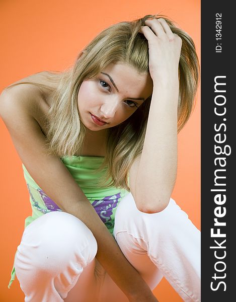 Blond girl relaxing with a hand in her hair; wearing casual clothes; orange background. Blond girl relaxing with a hand in her hair; wearing casual clothes; orange background