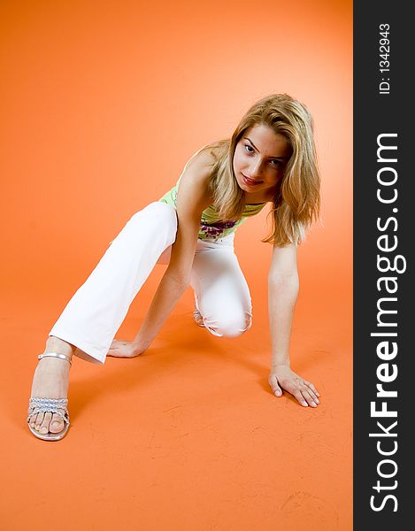 Blond girl doing some exercises; wearing casual clothes; orange background. Blond girl doing some exercises; wearing casual clothes; orange background