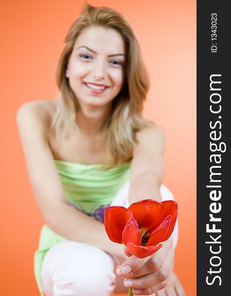 Beautiful blond girl offering a red tulip to someone, smiling and looking happy orange background. Beautiful blond girl offering a red tulip to someone, smiling and looking happy orange background