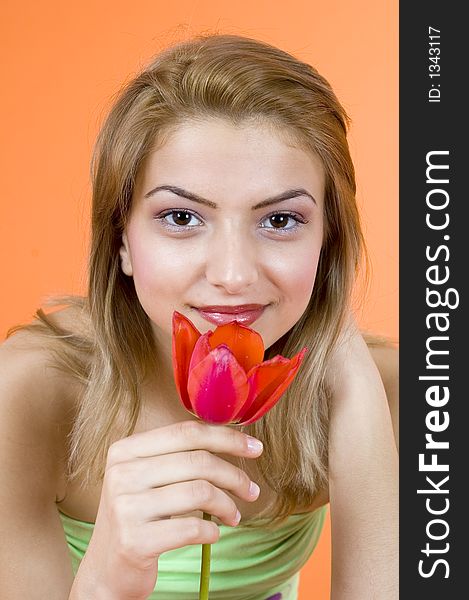 Beautiful blond girl smelling a red tulip and looking relaxed; orange background. Beautiful blond girl smelling a red tulip and looking relaxed; orange background