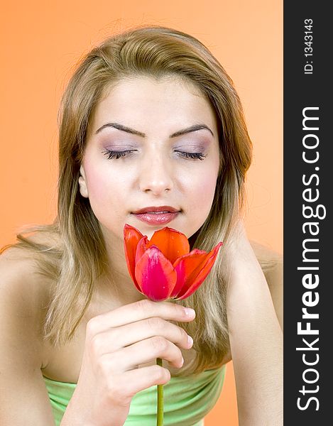 Beautiful blond girl smelling a red tulip with her eyes closed, looking relaxed; orange background. Beautiful blond girl smelling a red tulip with her eyes closed, looking relaxed; orange background