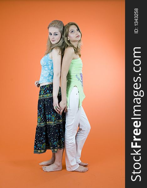 Two beautiful blond girls standing back to back and holding their hands; orange backgroung. Two beautiful blond girls standing back to back and holding their hands; orange backgroung