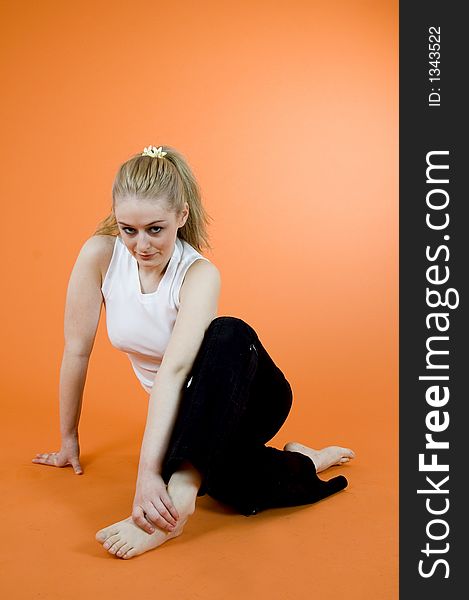 Young and beautiful blond girl wearing sport clothes and exercising; posing in a studio; isolated on orange background. Young and beautiful blond girl wearing sport clothes and exercising; posing in a studio; isolated on orange background