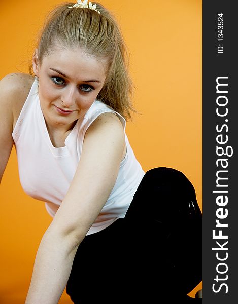 Young and beautiful blond girl wearing sport clothes and exercising; posing in a studio; isolated on orange background. Young and beautiful blond girl wearing sport clothes and exercising; posing in a studio; isolated on orange background