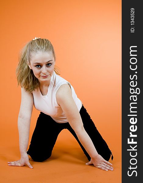 Young and beautiful blond girl wearing sport clothes and exercising; posing in a studio; isolated on orange background. Young and beautiful blond girl wearing sport clothes and exercising; posing in a studio; isolated on orange background