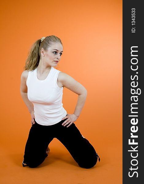 Young and beautiful blond girl wearing sport clothes and exercising; posing in a studio; isolated on orange background. Young and beautiful blond girl wearing sport clothes and exercising; posing in a studio; isolated on orange background