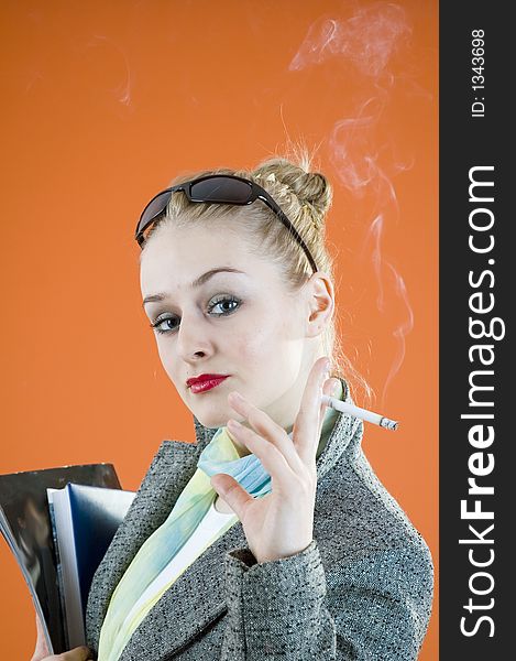 Portrait of a beautiful young blond with glamour look and make-up holding some books and smiking a cigar; isolated on orange. Portrait of a beautiful young blond with glamour look and make-up holding some books and smiking a cigar; isolated on orange