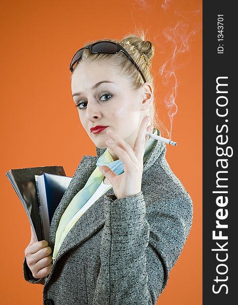 Portrait of a beautiful young blond with glamour look and make-up holding some books and smiking a cigar; isolated on orange. Portrait of a beautiful young blond with glamour look and make-up holding some books and smiking a cigar; isolated on orange