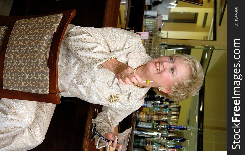 A well dressed smiling senior woman having a drink at a bar looking away. A well dressed smiling senior woman having a drink at a bar looking away.