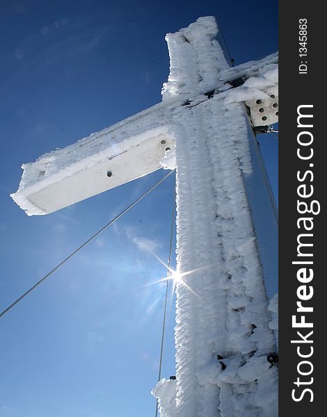 Frozen mountain cross with sun on its edge