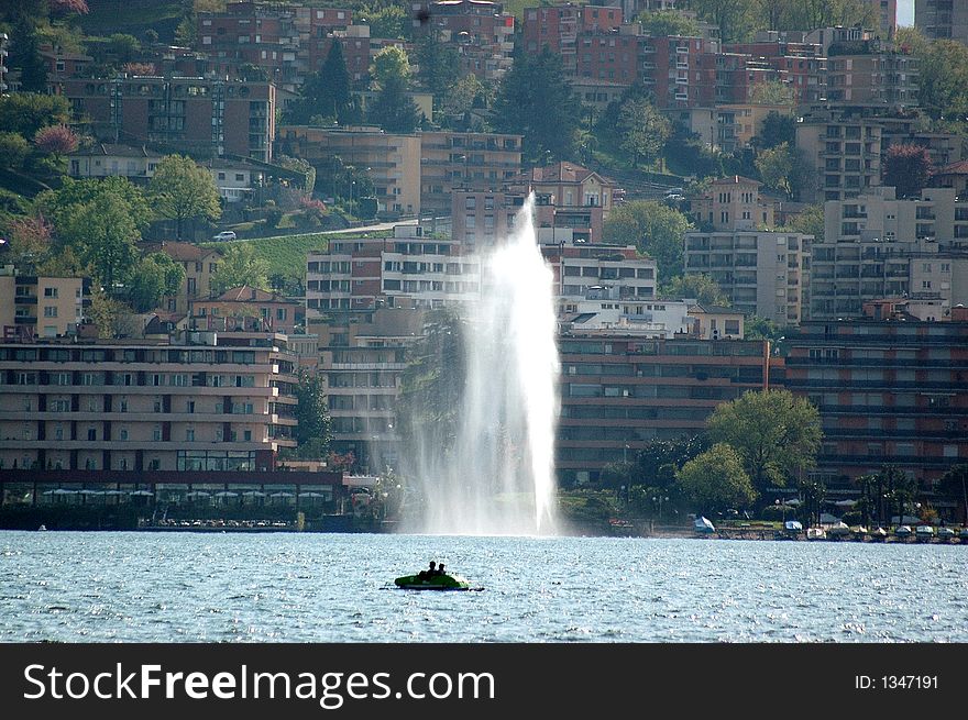 Lake of lugano in a sunny day with a boat and a fountain. on the background Lugano Paradiso. Lake of lugano in a sunny day with a boat and a fountain. on the background Lugano Paradiso