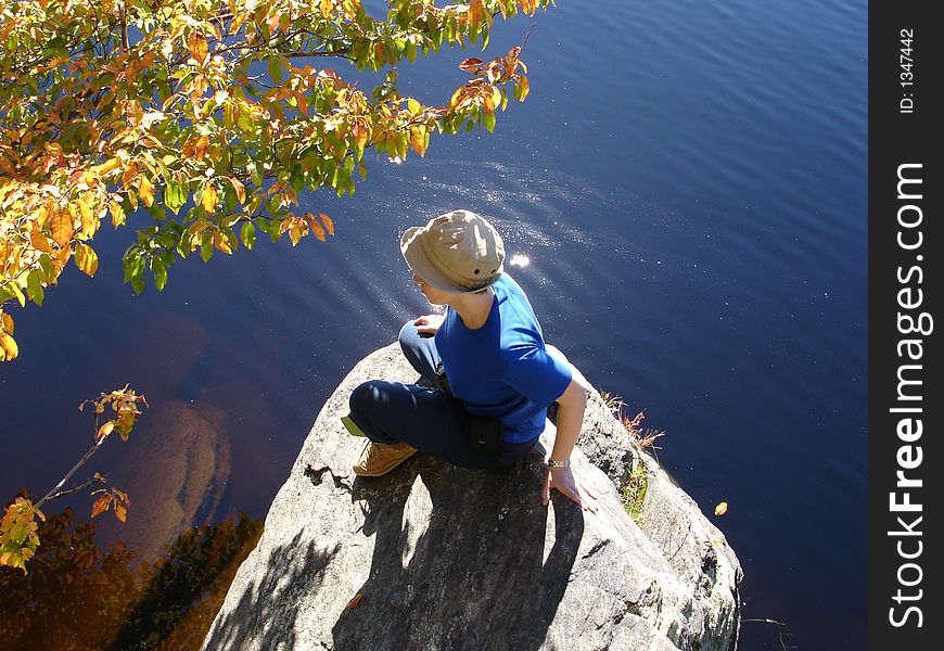 Girl sits ashore on large stone. Harriman state park, NY, Island pond