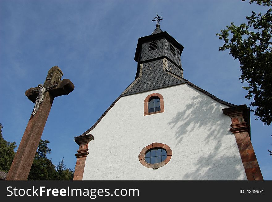 A view of an old German Catholic church and a crucifix cross in Hohenecken, Germany. A view of an old German Catholic church and a crucifix cross in Hohenecken, Germany
