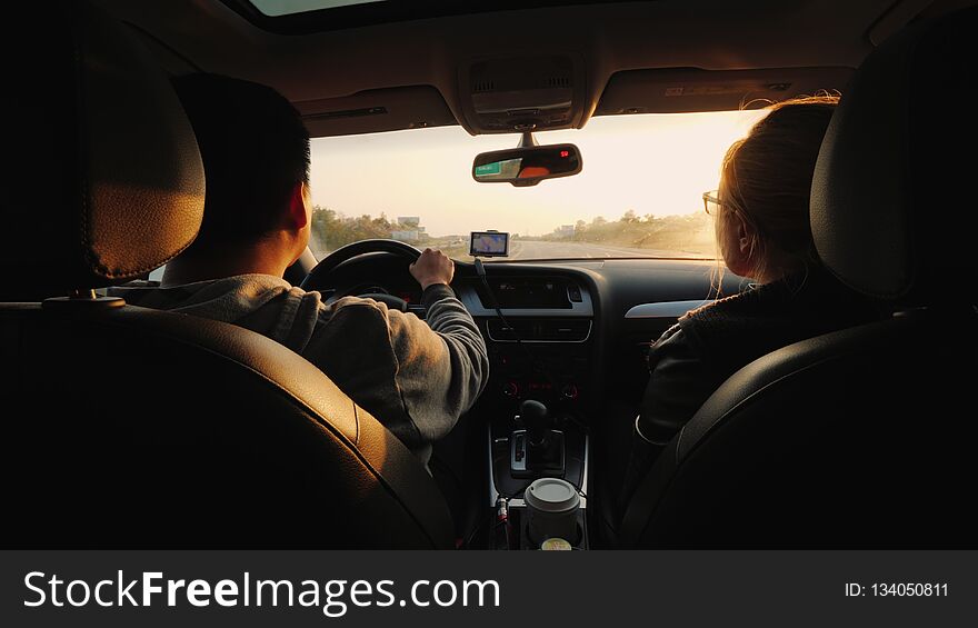 A married couple travels by car, the setting sun illuminates them. Asian man driving