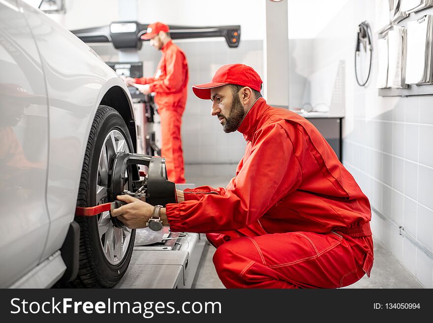 Handsome auto mechanic in red uniform fixing disk for wheel alignment at the car service. Handsome auto mechanic in red uniform fixing disk for wheel alignment at the car service