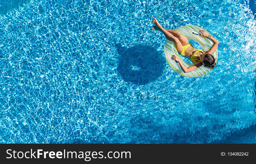 Aerial drone view of little girl in swimming pool from above, kid swims on inflatable ring donut , child has fun in blue water