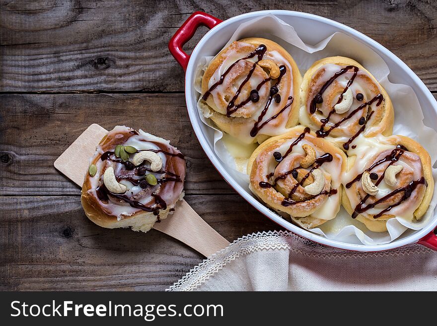 Cinnabon with cream cheese, chocolate and cashew nuts on wooden background
