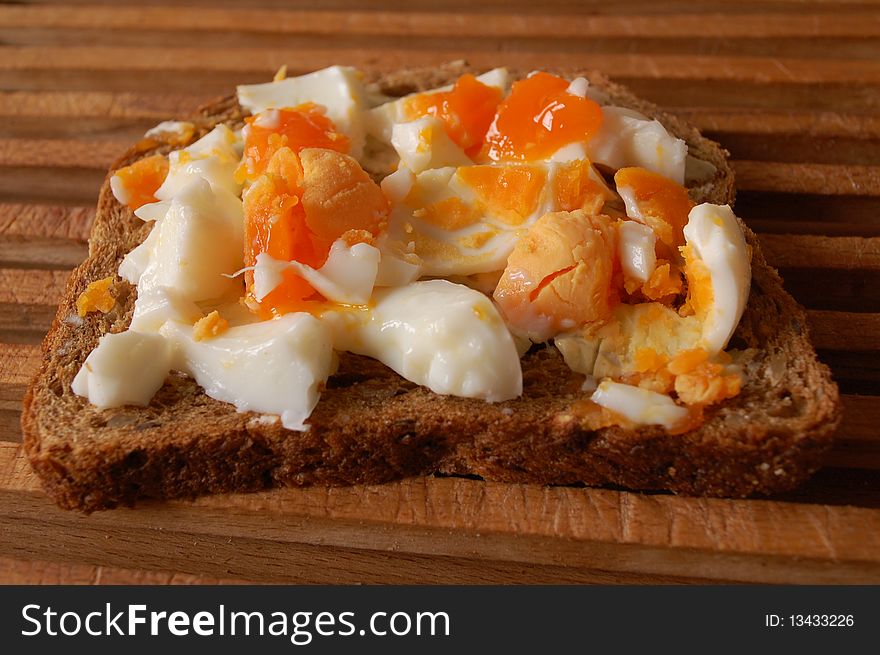 A brown sandwich with boiled eggs on a wooden plate. A brown sandwich with boiled eggs on a wooden plate