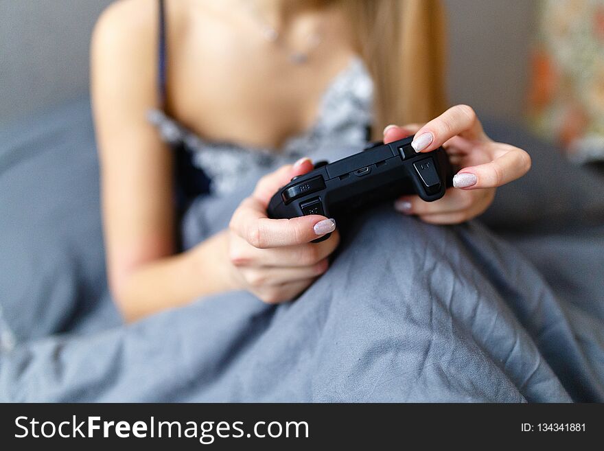 Girl gamer playing video game with wireless joystick at home. Gamepad in female hands close-up, gaming addiction concept, woman gamer in underwear relaxes in the bed