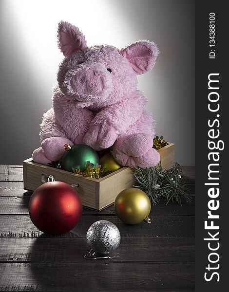 Toy pig sitting on box with New year balls on wooden surface. Festive card, Chinese New Year of Pig, Zodiac symbol 2019