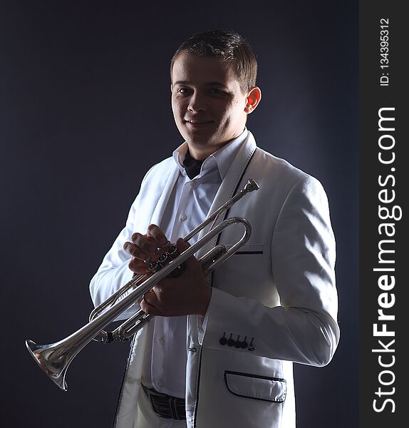 Young Man In A White Suit With A Trumpet.isolated On Black Background