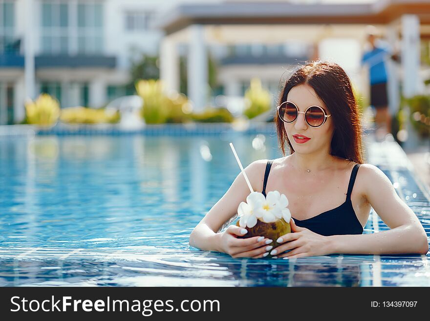 Brunette girl drinking coconut juice by the pool