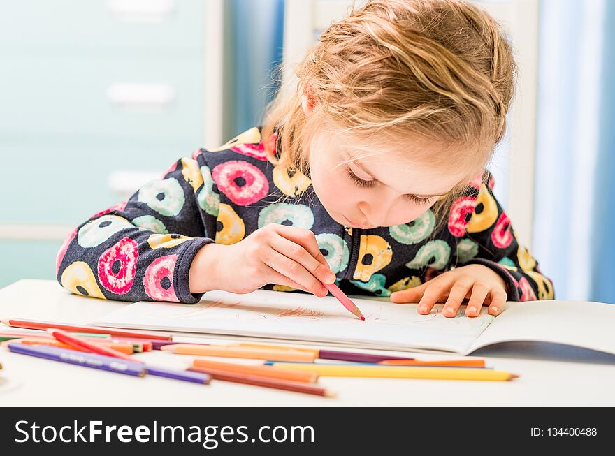 Little blonde girl draws with pencils