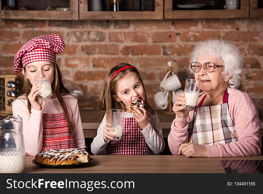 Caring granny with two little granddaughters drinking milk and tasting homemade pie. Caring granny with two little granddaughters drinking milk and tasting homemade pie