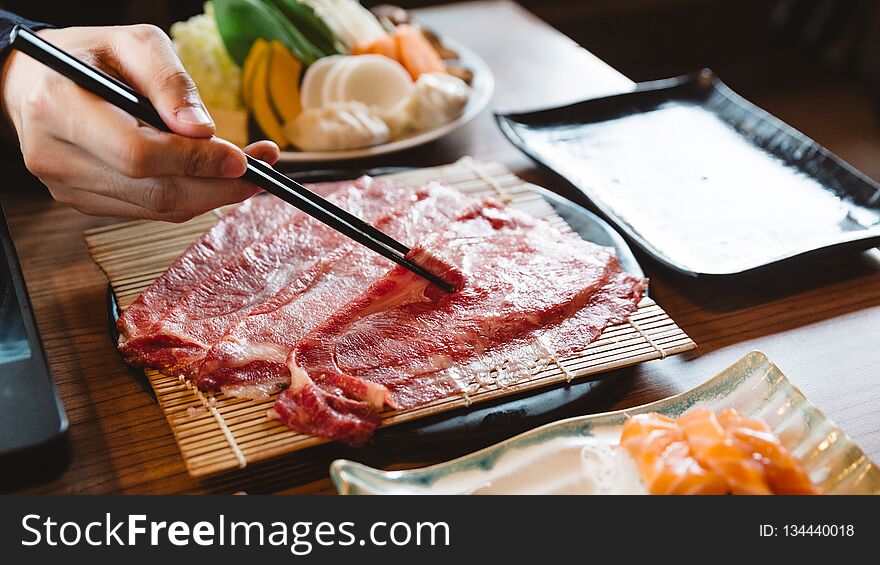 Man holding rare slice Wagyu A5 beef by chopsticks for boiling in Shabu hot pot