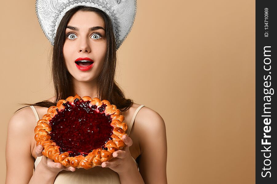 Shocked beauty russian woman in kokoshnik hat, has cake during dinner time, being surprised