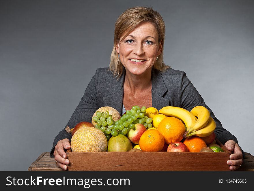 Many fruits stacked together and cute woman bearing them. Many fruits stacked together and cute woman bearing them