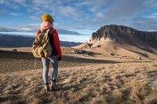 Portrait From The Back Of A Girl Traveler In A Jacket With A Cap And A Backpack Stands On The Background Of An Epic Stock Photo