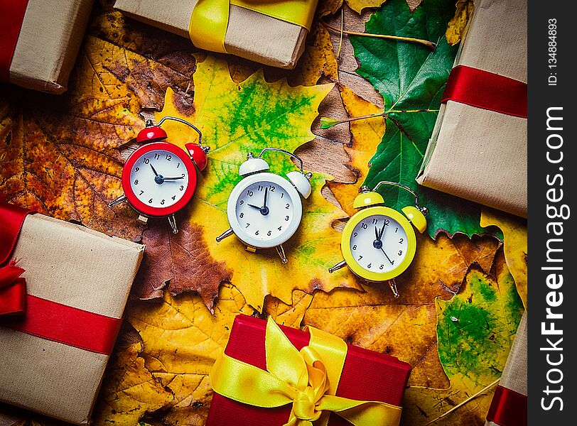 Vintage alarm clocks and maple leaves with Holiday gifts on wooden background