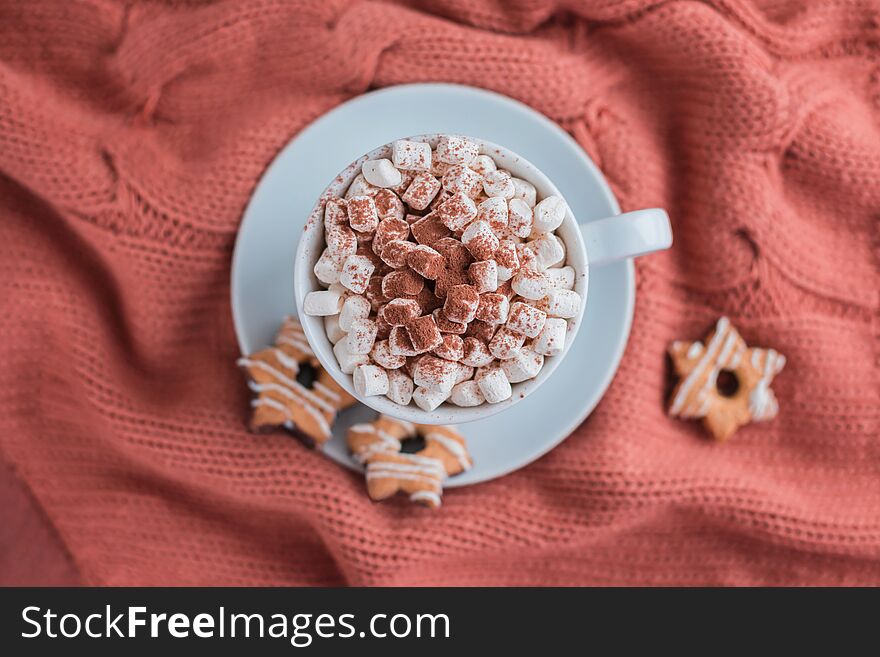 Coffee cup with marshmallow and stars cookies on warm knitted coral blanket