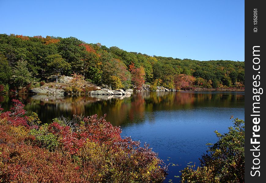 Small pond in Harriman state park, NY. Hikers rest after long hike. Fall forest reflects on the pond's waters.