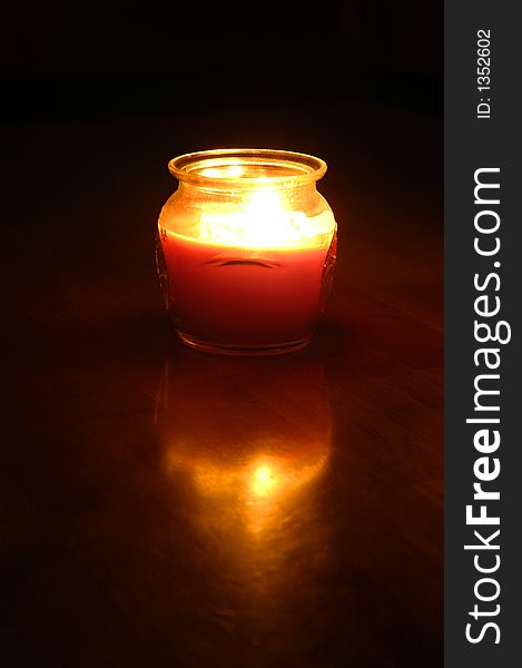 Candle glowing on wood surface with reflection