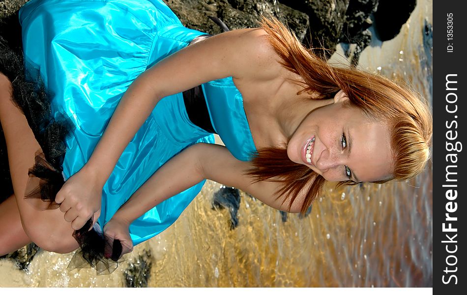 A pretty teen sitting on the rocks at the beach in a formal dress. A pretty teen sitting on the rocks at the beach in a formal dress.