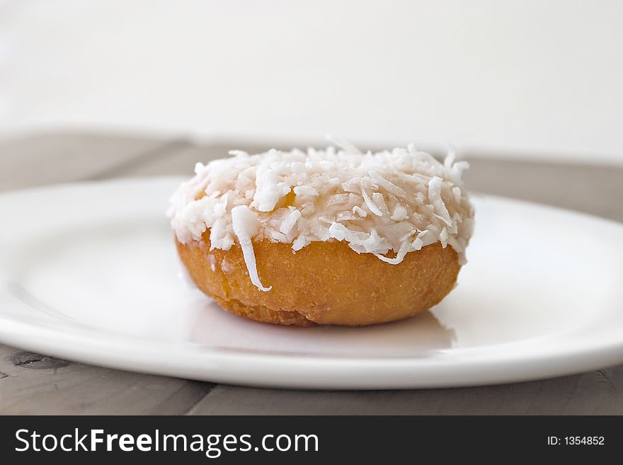 Single coconut-covered donut on white plate