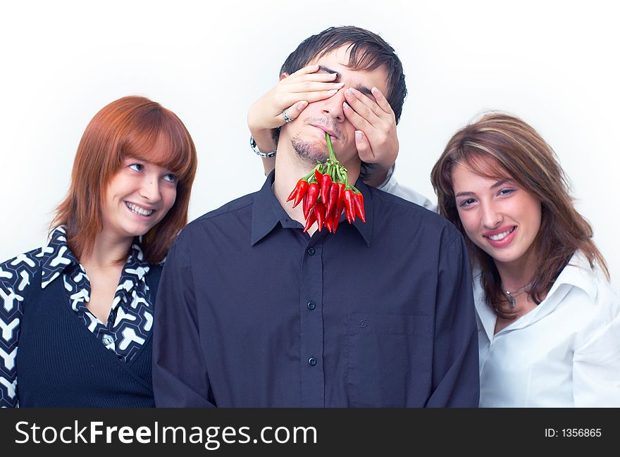 Guy holding a bunch of red chilli peppers in his mouth and two beautiful girls covering his eyes with the hands. Guy holding a bunch of red chilli peppers in his mouth and two beautiful girls covering his eyes with the hands