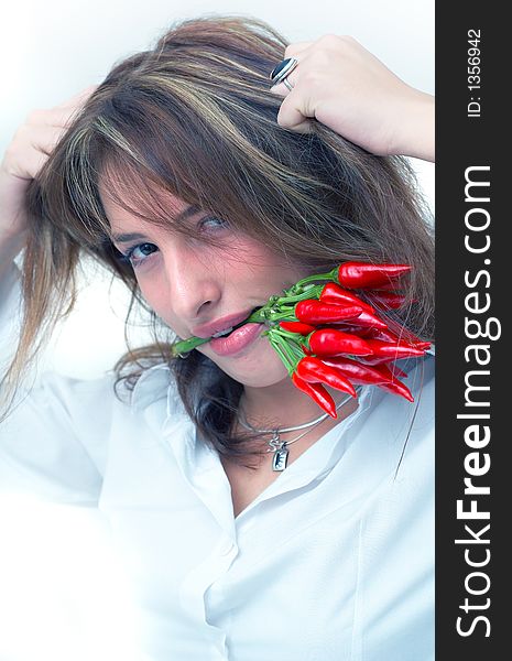 Portrait of a beautiful young girl holding a bunch of chilli peppers in her mouth and pulling on her hair. Portrait of a beautiful young girl holding a bunch of chilli peppers in her mouth and pulling on her hair
