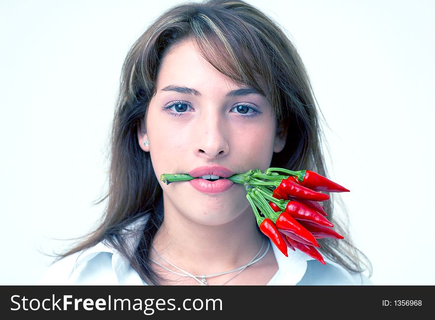 Portrait of a beautiful young girl holding a bunch of red chilli peppers in her mouth; white background. Portrait of a beautiful young girl holding a bunch of red chilli peppers in her mouth; white background