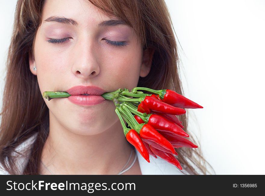 Portrait of a beautiful young girl holding a bunch of red chilli peppers in her mouth; white background. Portrait of a beautiful young girl holding a bunch of red chilli peppers in her mouth; white background