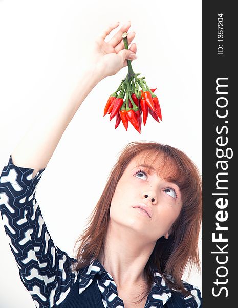 Portrait of a beautiful young girl holding a bunch of red chilli peppers over her head and looking at them; white background. Portrait of a beautiful young girl holding a bunch of red chilli peppers over her head and looking at them; white background