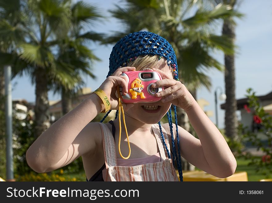 A 7 years old playing with a toy camera with palm trees as background and sunny sky. A 7 years old playing with a toy camera with palm trees as background and sunny sky