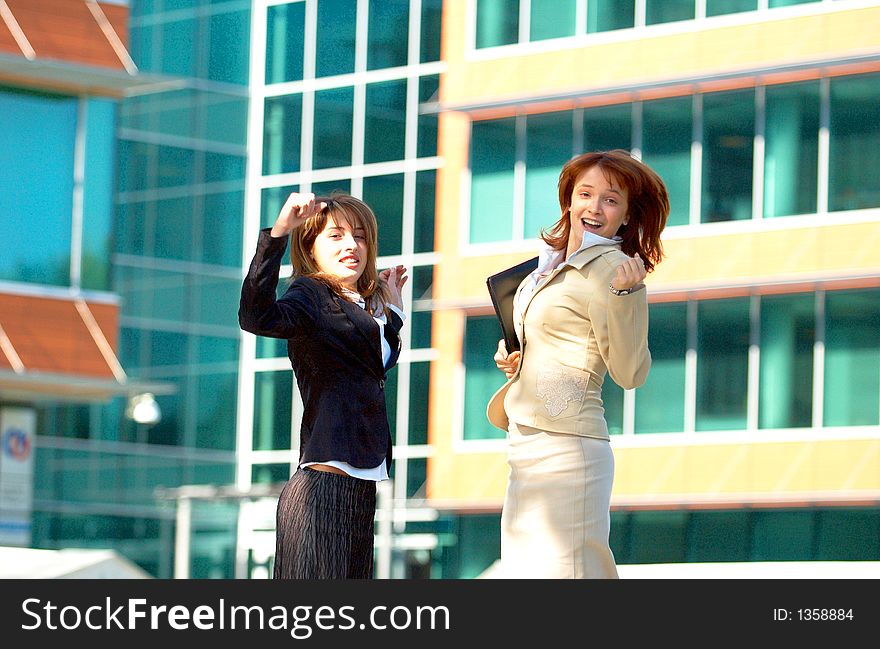 Two beautiful business women jumping in front of a business building, being happy for their success. Two beautiful business women jumping in front of a business building, being happy for their success