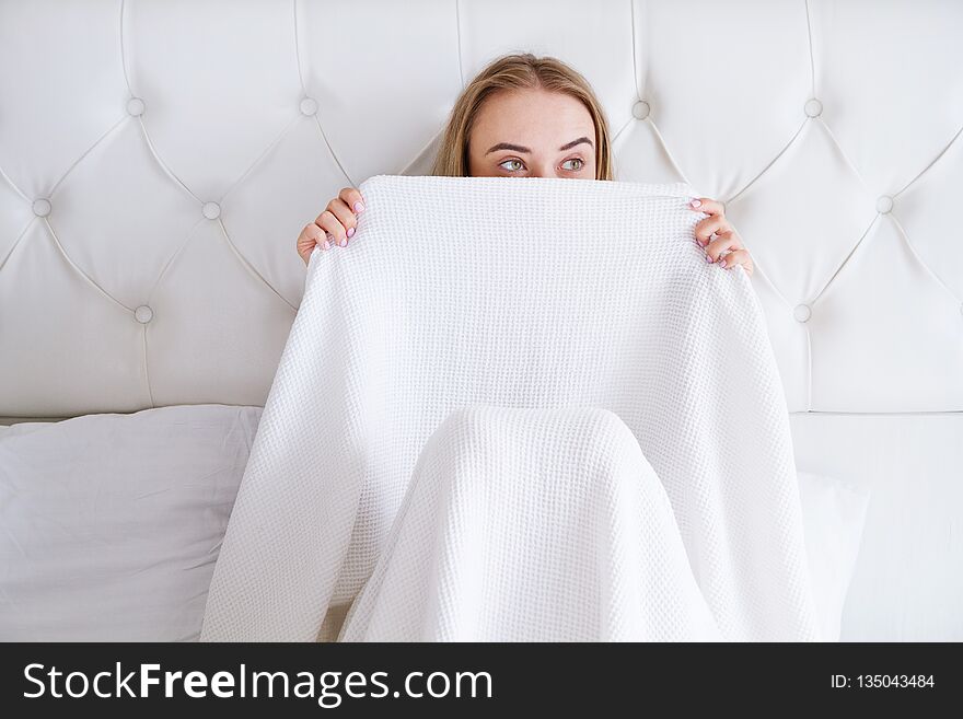 Pretty young woman with white hair hiding face behind blanket in the morning bedroom, comic girl