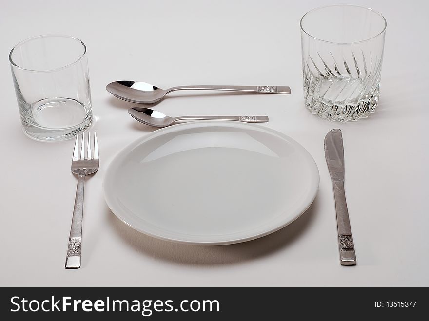 Two glasses with a white plate and two spoons and knife and fork. Two glasses with a white plate and two spoons and knife and fork