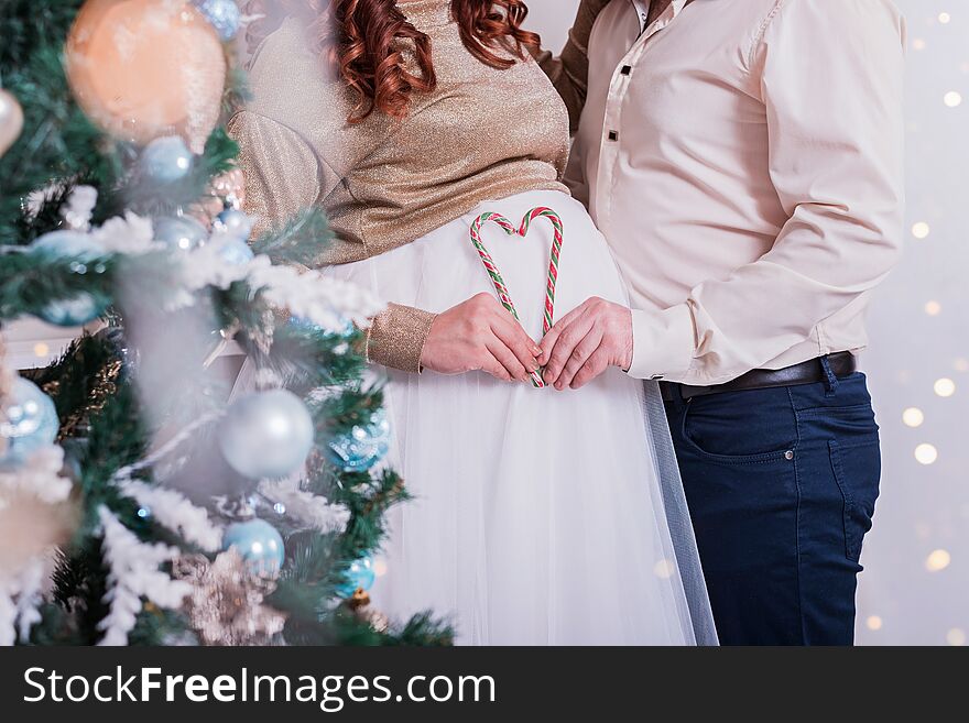 Couple makes heart with candy canes on background of a pregnant belly